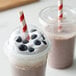 Two plastic cups with EcoChoice giant red and white striped paper straws in smoothies with blueberries and strawberries.