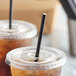 A close-up of two plastic cups with black EcoChoice paper straws and plastic lids.