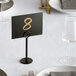 A table with a white plate, a glass, and a black table number in a Choice 6" Black Menu / Card Holder.