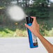 A hand holding a blue Weiman spray can and spraying a window.