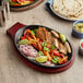 A Choice oval cast iron fajita skillet with meat and vegetables on it, with tortillas on the side.