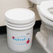 A white bucket with a lid of Noble Chemical Refresh Concentrated Deodorizing Fluid next to a toilet.