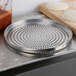 An American Metalcraft aluminum pizza pan with holes in it next to dough and a cutting board.