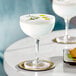 Two Acopa Deco coupe cocktail glasses of white liquid on a table with food.