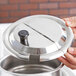 A person holding a stainless steel notched lid for a silver pot.