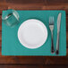 A white plate, fork, and knife on a teal Hoffmaster paper placemat with scalloped edges.