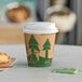 An EcoChoice paper coffee cup with a tree print on it and a lid on a table with a croissant.