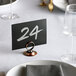 An antique bronze table card holder with a place card displaying the number 24.
