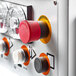 A close up of a control panel with a red button and yellow circular button on a black and orange Avancini dough mixer.