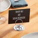 A Choice chrome table card holder with a round base holding a sign on a table.