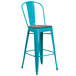 A turquoise metal bar stool with a wooden seat.