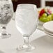 A clear 14 oz. glass goblet filled with ice water, placed on a table.