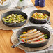 Three Valor pre-seasoned cast iron skillets with sausages and vegetables on a table.