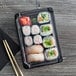 A tray of sushi rolls in Eco-Products small sushi containers with chopsticks on a wood table.