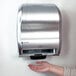 A person using a San Jamar hands free paper towel dispenser on a wall.