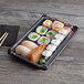 A tray of sushi rolls in a large white plastic container with a clear lid.