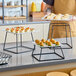 A three-piece set of square black metal display stands with white plates holding assorted appetizers.