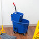 A blue Rubbermaid WaveBrake mop bucket with a mop on the floor.