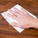 A hand using a Chicopee white medium-weight wiper to clean a surface.
