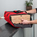 A person putting pizza boxes in a red Cambro pizza delivery bag.