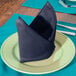A folded Intedge navy blue cloth napkin on a plate.