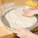 A person's hand rolling pizza dough in an American Metalcraft tapered pizza pan.