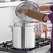 A person using a glove to put a lid on a Choice aluminum stock pot.