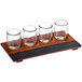 An Acopa wood tray with four rounded tasting glasses on a table.