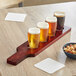 An Acopa mahogany wood flight paddle holding Barbary tasting glasses of beer on a table.