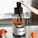 A woman using a Waring commercial food processor to chop carrots.