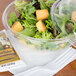 A Dart clear plastic bowl filled with salad with a dome lid.