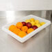 A white Rubbermaid food storage box on a counter filled with oranges and apples.