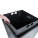 A hand placing a black rectangular trash can with a stainless steel lid on a counter.
