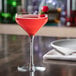 A Libbey Prism Coupe Glass filled with pink liquid and a cherry on top on a table.