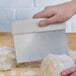 A hand using a Dexter-Russell stainless steel dough cutter to cut dough.