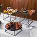 A black table with Acopa Slate risers holding plates of food.