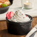 A black stoneware ramekin filled with whipped cream and garnished with sliced strawberries.