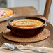 A brown porcelain onion soup crock filled with soup and topped with toasted bread.