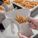 A person using a Vollrath dual handle French fry scoop to fill a bag with fries.