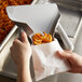 A hand using a Vollrath plastic dual handle curly fry scoop to fill a white paper bag with fries.