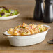 An Acopa vanilla bean stoneware oval casserole dish filled with macaroni and cheese on a table.