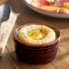 A brown porcelain ramekin filled with a baked dish, garnished with herbs.