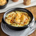 A black porcelain onion soup crock filled with baked soup topped with melted cheese and croutons.