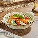 A vanilla bean porcelain shirred egg casserole dish filled with a fresh salad, featuring sliced peaches, mozzarella, greens, and basil.