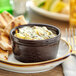 A bowl of dip in an Acopa chestnut stoneware ramekin on a table with crackers and pita.