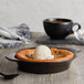 A black Acopa stoneware dish with a bowl of food and a scoop of ice cream on top.