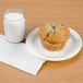 A muffin on a plate next to a Carlisle clear plastic tumbler filled with milk.