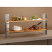 A Rosseto stainless steel riser stand holding food on a wooden shelf.