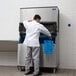 A man in a white shirt and black jacket standing next to a blue Manitowoc ice machine bin.