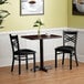 A Lancaster Table & Seating black table with two chairs set in a room with a plant and a picture on the wall.